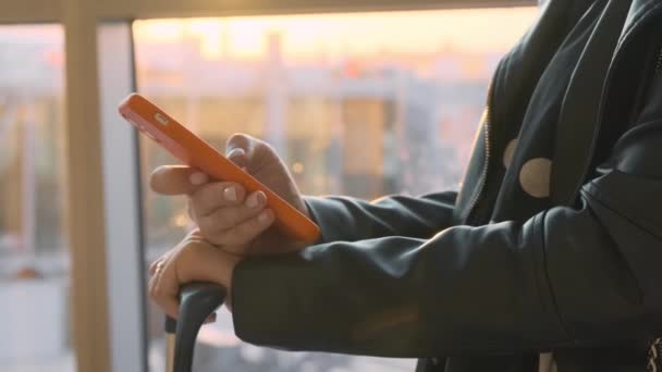 A közeli nő keze egy mobiltelefont használ, ami a reptér ablaka mellett áll a napfénynél..  - Felvétel, videó