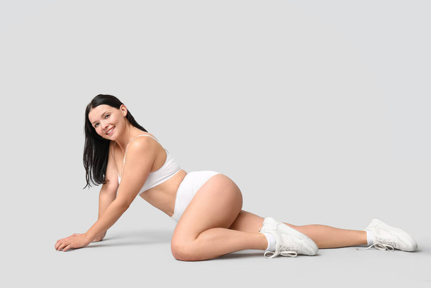Body positiivinen nainen alusvaatteet istuu kevyellä taustalla - Valokuva, kuva