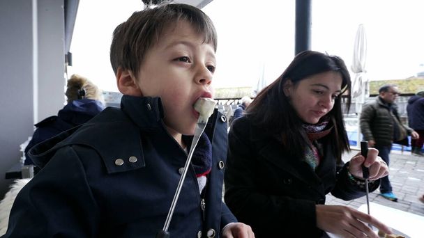 Madre e hijo disfrutando de fondue suiza en el restaurante mientras viajan de vacaciones. Primer plano del niño soplando en el pan con queso - Foto, imagen