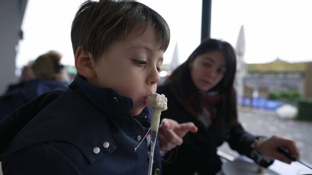 Kind kühlt heißes Schweizer Fondue, Essen im Restaurant mit Mama - Foto, Bild