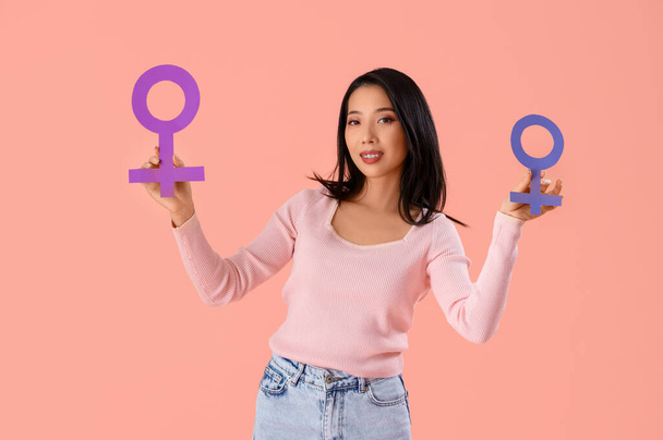 Młoda Azjatka z symbolami płci na różowym tle - Zdjęcie, obraz