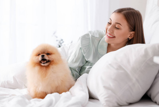 Mujer joven con lindo perro de Pomerania acostado en el dormitorio - Foto, Imagen