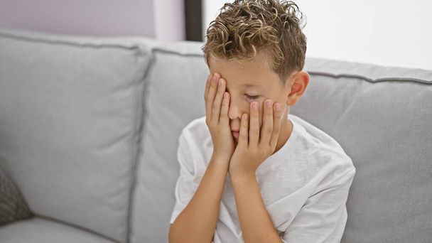 Rozkošné blonďaté dítě sedící v zoufalství na pohovce doma, sužované stresem a frustrací - Fotografie, Obrázek