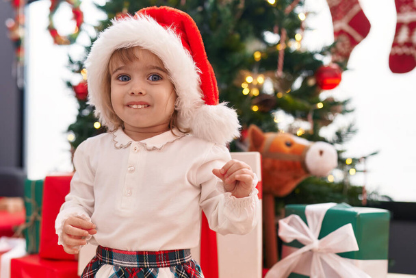 Adorável menina loira sorrindo confiante em pé pela árvore de Natal em casa - Foto, Imagem