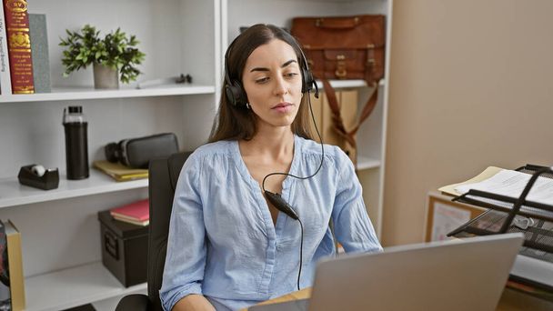 Houkutteleva nuori latino nainen, menestyksen ruumiillistuma, rentoutuminen hänen toimistopöydällään, lukittu hänen työhönsä kannettavalla tietokoneella kuulokkeilla, täysin omistaen yritysmaailman! - Valokuva, kuva