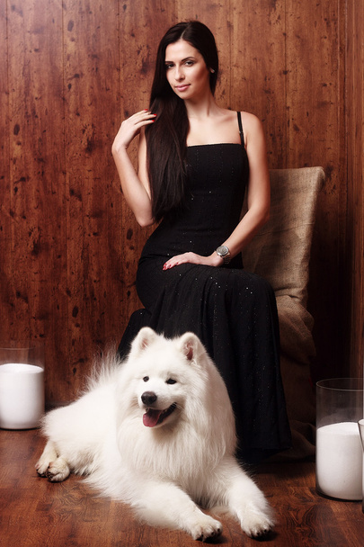 beautiful brunette young woman long black dress with a snow-white dog Samoyed husky studio in shades of brown candles - Photo, Image