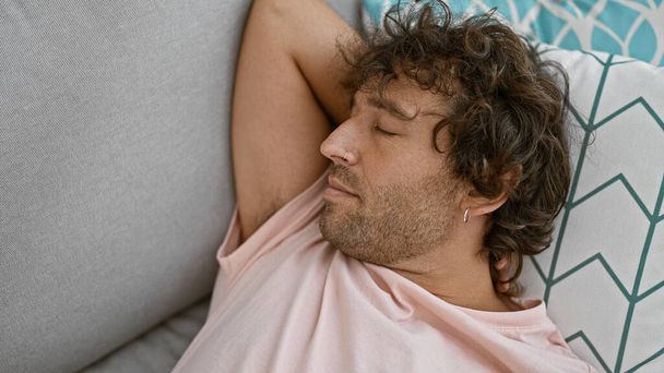 Kıvırcık saçlı genç bir adam rahat bir ev ortamında kanepede huzur içinde uyur. - Fotoğraf, Görsel