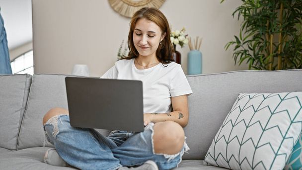 Młoda kobieta za pomocą laptopa siedzi na kanapie w domu - Zdjęcie, obraz