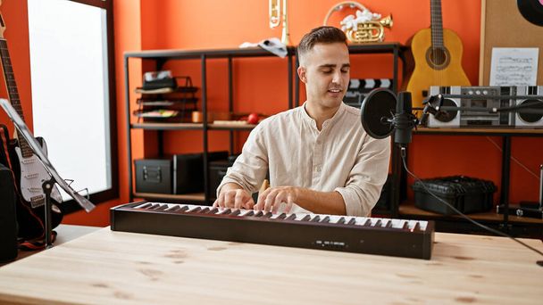 Egy fiatal spanyol férfi játszik billentyűzeten egy narancs zenei stúdióban, tele hangszerekkel.. - Fotó, kép