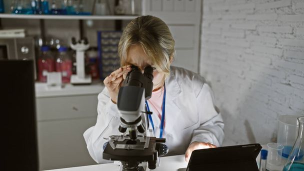 Kavkazská vědkyně pečlivě analyzuje vzorek pomocí mikroskopu v dobře vybavené laboratoři uvnitř. - Fotografie, Obrázek