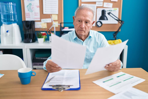 Grauhaariger Mann mittleren Alters liest im Büro Dokument - Foto, Bild