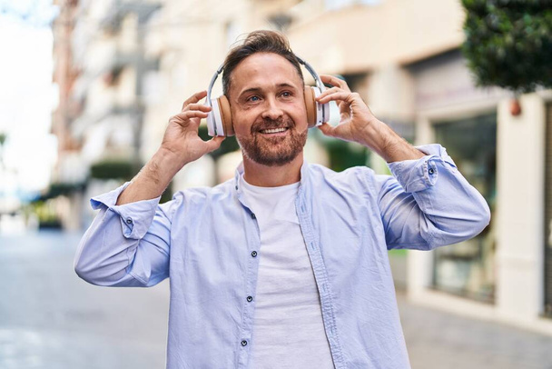 Jovem caucasiano sorrindo confiante ouvir música na rua - Foto, Imagem