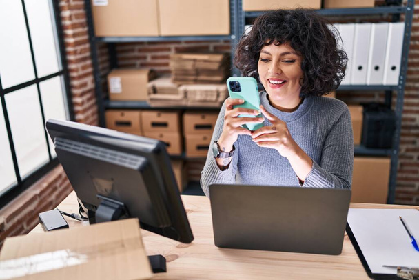 Молода красива іспанська жінка електронної комерції бізнес-працівник використовує ноутбук і смартфон в офісі
 - Фото, зображення