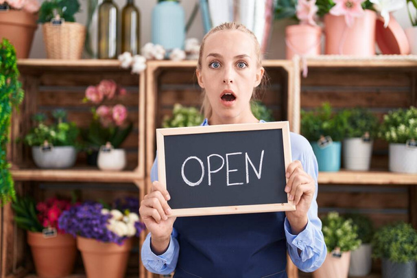 Young caucasian woman working at florist holding open sign afraid and shocked with surprise and amazed expression, fear and excited face.  - Photo, Image