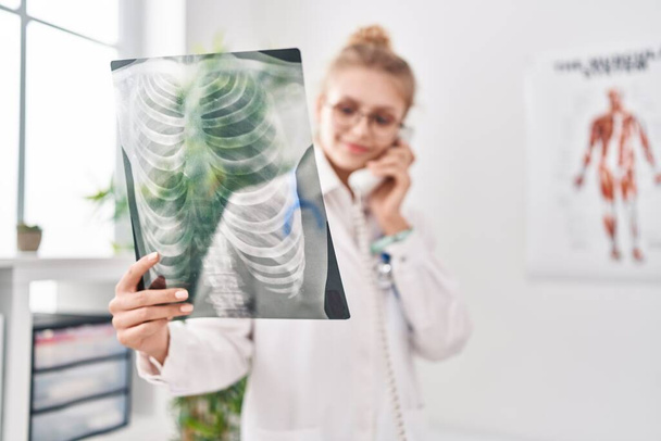 Fiatal szőke nő orvos beszél telefonon tartja röntgen klinikán - Fotó, kép