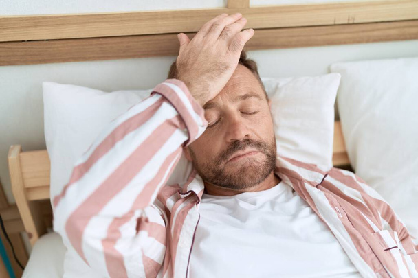 Middelbare leeftijd man lijden aan hoofdpijn liggend op bed in de slaapkamer - Foto, afbeelding