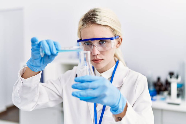 Jeune femme blonde scientifique versant du liquide sur éprouvette au laboratoire - Photo, image