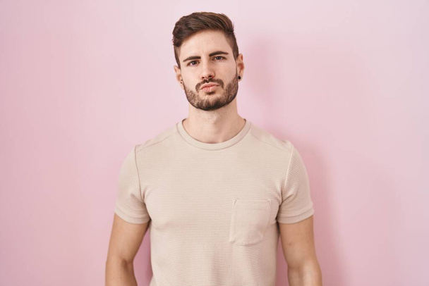 Een Spaanse man met een baard die over een roze achtergrond staat te kijken naar de camera die een kus op de lucht blaast en die lief en sexy is. liefde uitdrukking.  - Foto, afbeelding