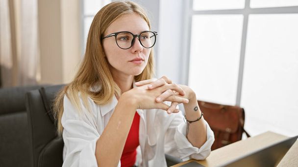 Вдумлива молода жінка в окулярах і світле волосся, розмірковуючи в офісі. - Фото, зображення