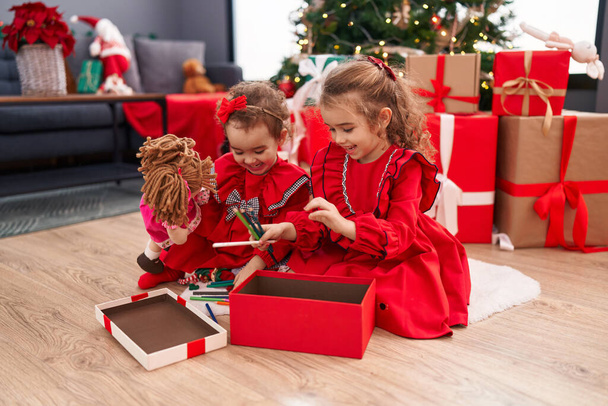 Adorable girls celebrating christmas unpacking pencils of gift at home - Photo, Image