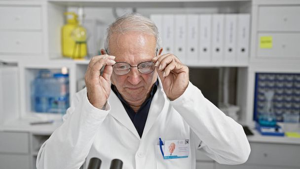 Serieuze senior wetenschapper, toegewijd aan geneeskunde, hout diep in de analyse. het dragen van een bril die moeizaam werkt in het lab met microscopie en biologie onderzoek. - Foto, afbeelding