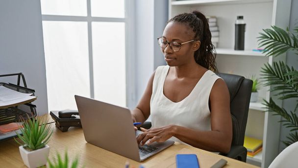 Egy afro-amerikai nő, aki figyelmesen dolgozik egy laptopon egy modern irodai környezetben.. - Fotó, kép