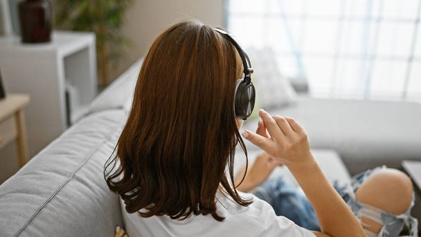 Young woman listening to music sitting on sofa at home - 写真・画像