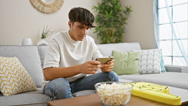Young hispanic teenager playing video game sitting on sofa at home - Photo, Image