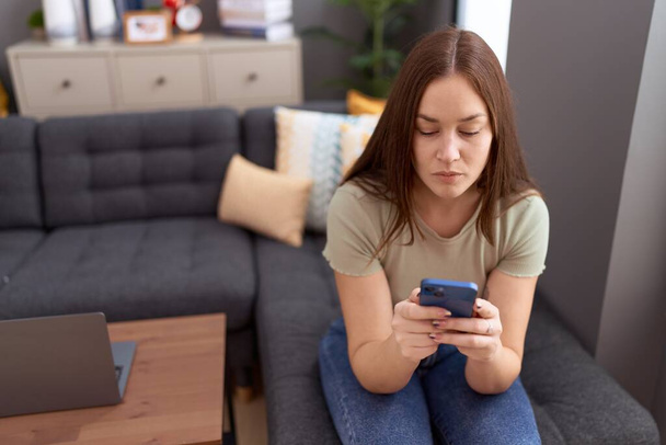 Junge schöne Frau nutzt Smartphone mit ernster Miene zu Hause - Foto, Bild