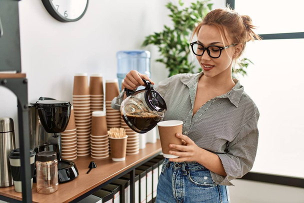Young caucasian woman business worker pouring coffee on take away glass at office - Photo, Image