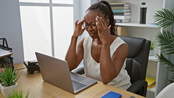 Eine professionelle afrikanisch-amerikanische Frau, die sich in einem modernen Büroumfeld im Haus gestresst fühlt. - Foto, Bild