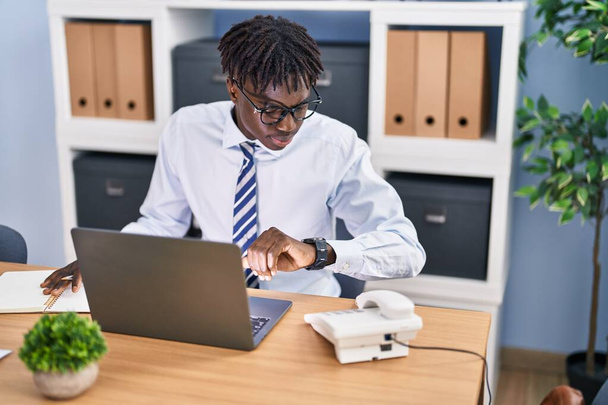 African american man business worker using laptop looking watch at office - Foto, Imagem