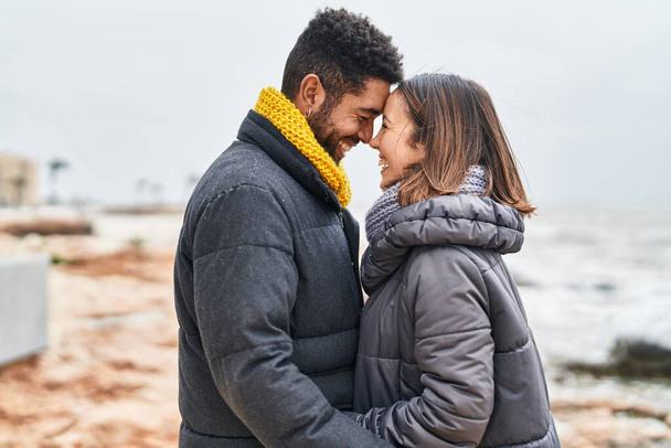 Мужчина и женщина улыбаются уверенно обнимая друг друга на берегу моря - Фото, изображение