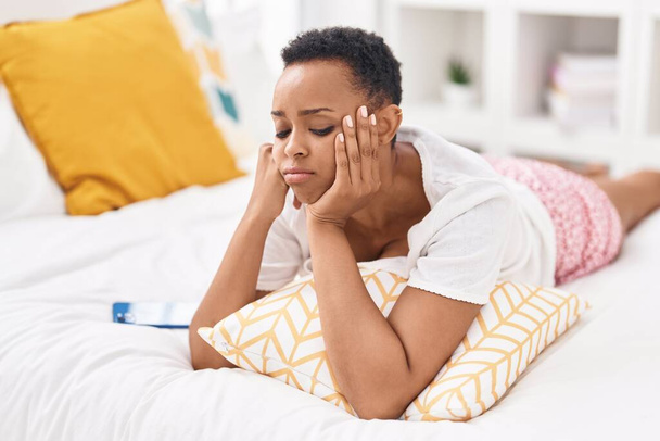 Donna afroamericana utilizzando smartphone con espressione preoccupata in camera da letto - Foto, immagini
