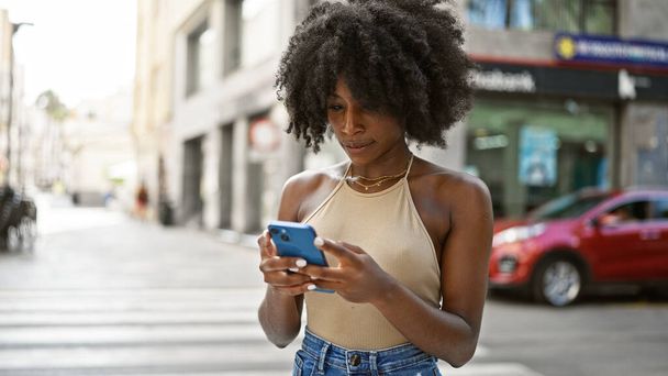 Mujer afroamericana usando smartphone con expresión seria en la calle - Foto, imagen