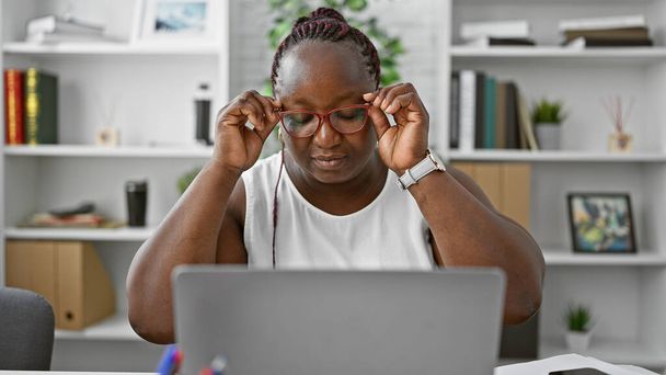 Συγκεντρωμένη Αφροαμερικάνα εργαζόμενη που αριστεύει στις επιχειρήσεις. εργάζεται επιμελώς στο laptop της, αυτή η κυρία αφεντικό ενσωματώνει την επιτυχία και τον επαγγελματισμό στο γραφείο της. - Φωτογραφία, εικόνα