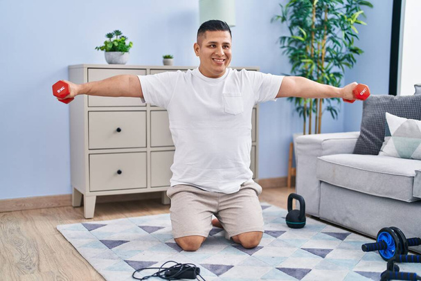Young latin man smiling confident using dumbbells training at home - Foto, Imagem