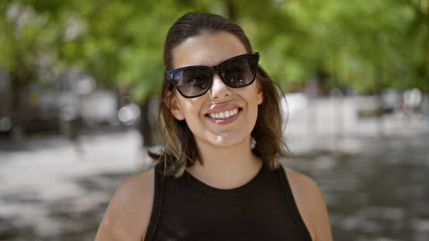 Souriante, belle femme hispanique, portant des lunettes se tient joyeusement dans les rues ensoleillées de Madrid, respirant la confiance à chaque pose. portrait urbain insouciant d'une vie adulte réussie. - Photo, image