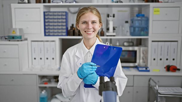 Una giovane scienziata sorridente che tiene una penna e degli appunti in un ambiente di laboratorio. - Foto, immagini