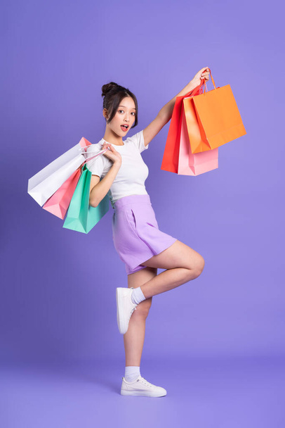 jong aziatisch vrouw holding shopping bag op paars achtergrond - Foto, afbeelding