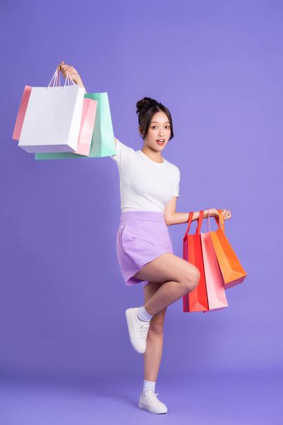 Joven mujer asiática sosteniendo bolsa de compras sobre fondo morado - Foto, imagen