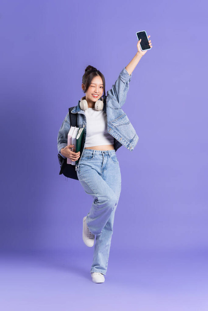 Portrait of a beautiful Asian schoolgirl wearing a backpack on a purple background - Photo, Image
