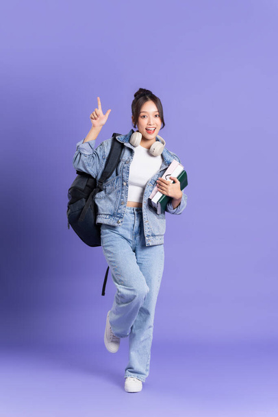 Retrato de uma bela estudante asiática usando uma mochila em um fundo roxo - Foto, Imagem