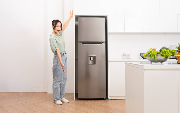 aziatische vrouw staan naast de koelkast in de keuken - Foto, afbeelding