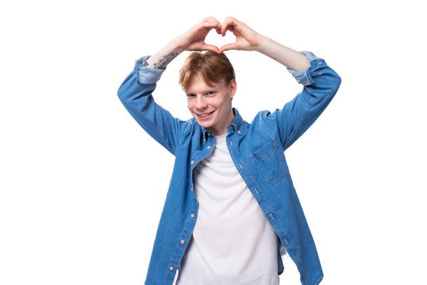 junger Mann mit roten Haaren im blauen Hemd zeigt ein Herz mit seinen Händen. - Foto, Bild