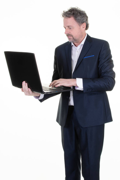 中年男性大人のハンサムなビジネスマンは,孤立した白い背景に立ってラップトップコンピュータで作業するスーツに着ています - 写真・画像