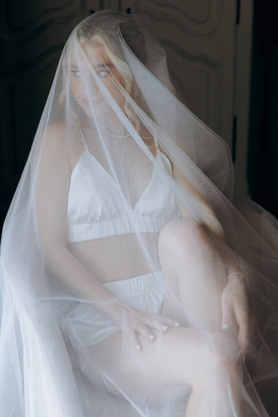 Πρωί της νύφης, όπου ετοιμάζεται για ένα γάμο σε ένα όμορφο πολυτελές ξενοδοχείο σε μια ρόμπα με κομψά μαλλιά και μακιγιάζ, και στη συνέχεια φοράει ένα λευκό νυφικό. - Φωτογραφία, εικόνα