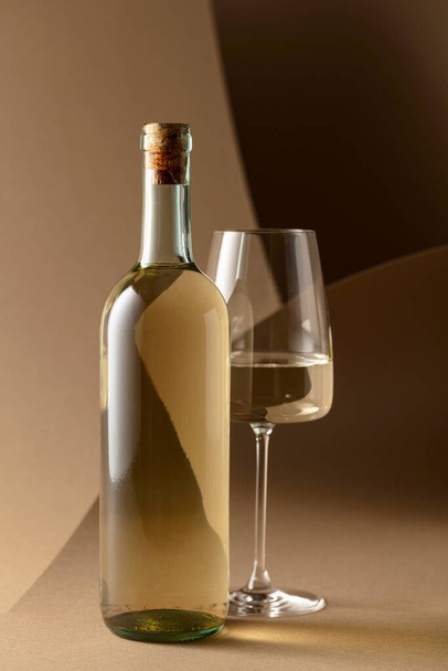 Botella y copa de vino blanco sobre fondo beige. - Foto, Imagen