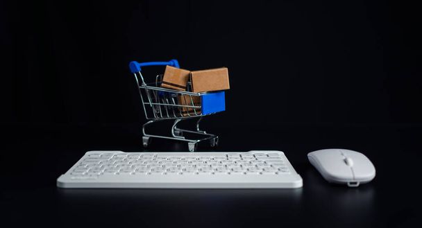 Boxes in a shopping car and keyboard on dark background. Ideas about online shopping, Online shopping for electronic commerce, Allows consumers to directly buy goods from seller over the internet. - Photo, Image