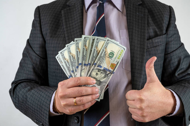  Молодой бизнесмен в костюме держит нам долларовые деньги. Финансовая концепция - Фото, изображение